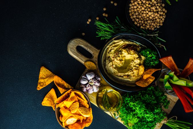 Top view of creamy hummus dip in bowl on board served with swirl of olive oil and chips