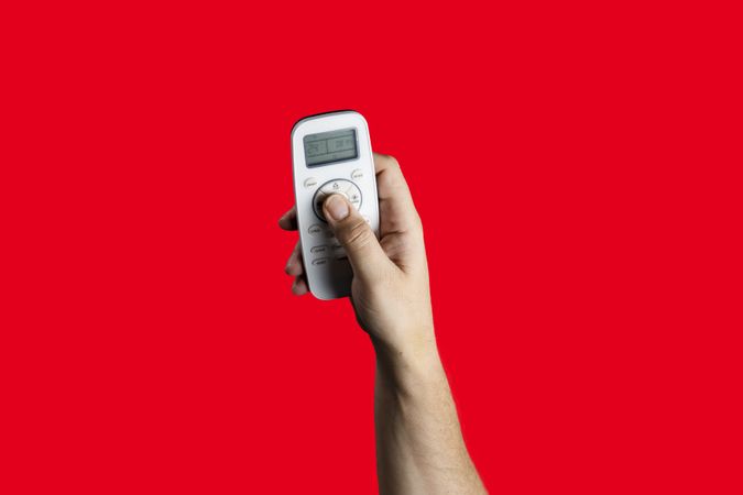 Hand holding an air conditioner remote control on a red background.