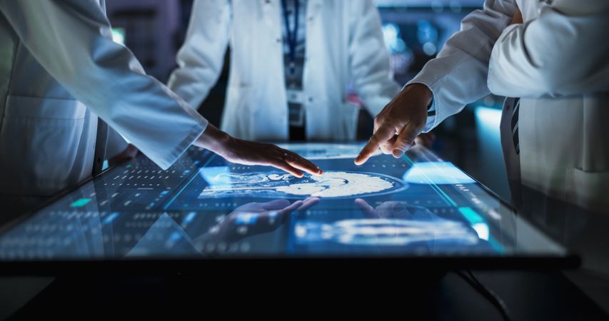 Hospital Medical Research Center: Focus On Hand Gestures Of Diverse Colleagues Gathered Around Interactive Touch Screen Table With MRI Scans Of Brain On Display.