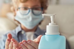 Crop child in mask applying sanitizer on hands