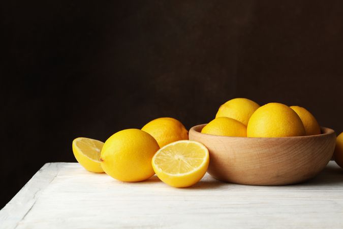 Wooden bowl and lemons against brown background, space for text