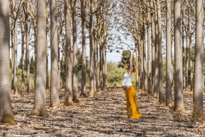 Adult expectant mother practicing yoga in park during sunny day