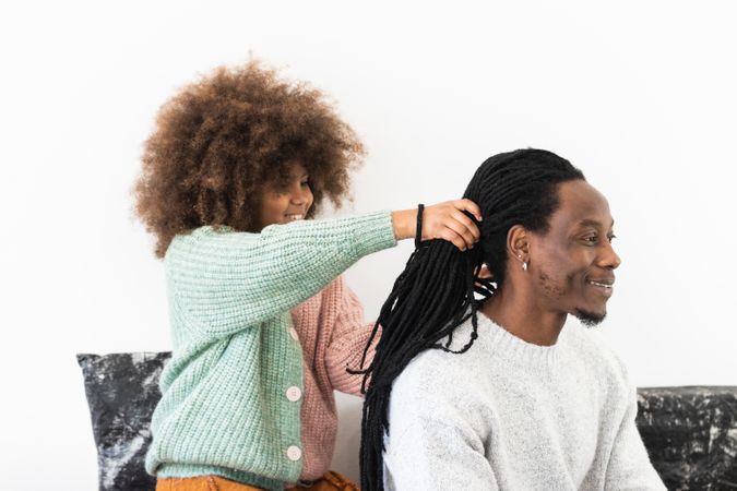 Amazed girl making hairdo on dreadlocks of father