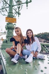 Smiling girlfriends sitting on green fence with lantern