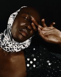 Man in dark polka dot shirt and headscarf against dark background