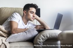Young man relaxing on sofa while using laptop 4BaJJE
