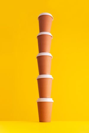 Single stack of disposable coffee cups on yellow background