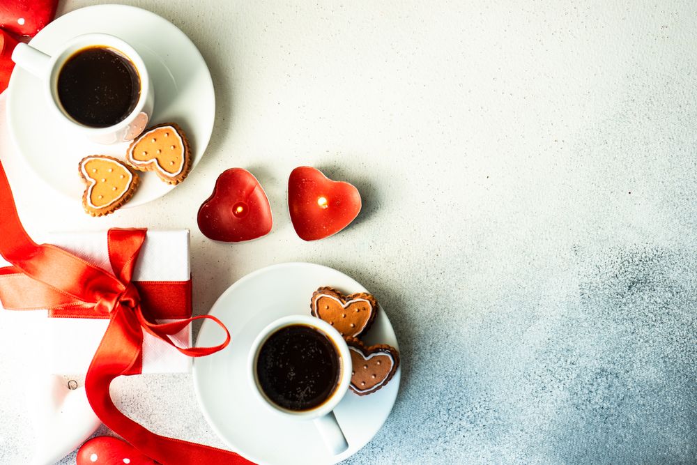Top view of two coffees with iced cookies and heart candles with space for text