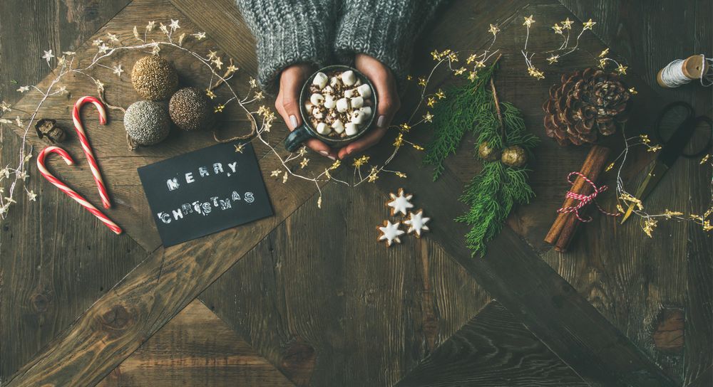 Homely holiday with “Merry Christmas” card, woman and hot chocolate, wide composition, copy space