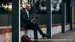 Businessman sitting outdoors with cell phone 4AOoY0