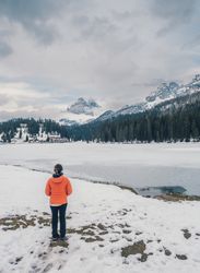 Unrecognizable person standing in snow surrounded by forest and mountains