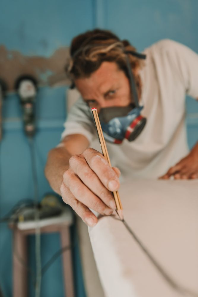 Man in respirator measuring surf board in workshop