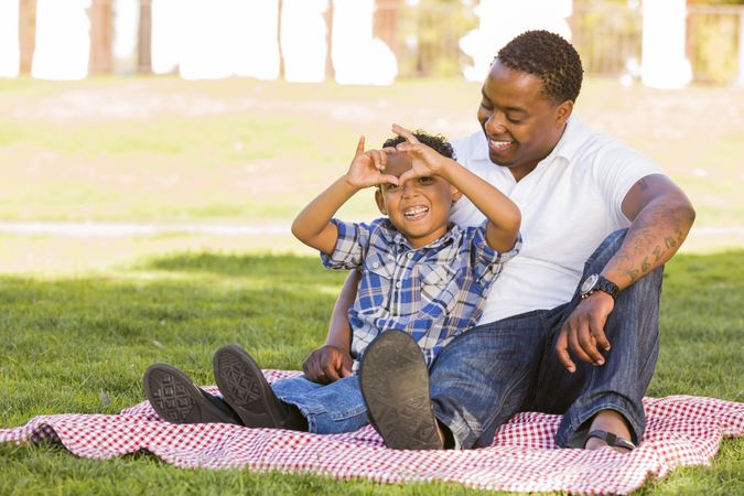 Father and Son Making Heart Hand Sign Sitting on the Grass