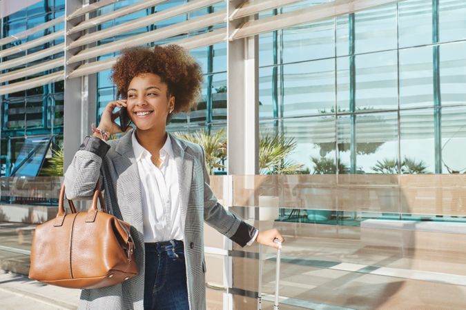 Smiling Black woman with luggage talking on smartphone
