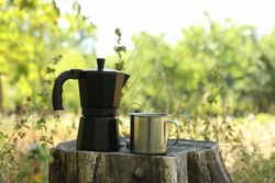 Coffee maker and metal cup on stump outdoor