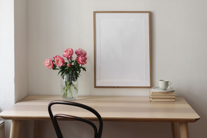 Elegant interior still life. Blank vertical picture frame mockup. Vase with pink peonies flowers. Cup of tea, coffee on books. Wooden table, desk. Romantic home breakfast.