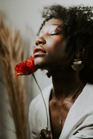 Woman with curly hair smelling red flower