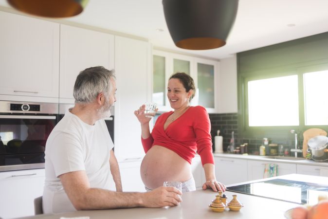Smiling laughing white couple, pregnant woman with husband in kitchen