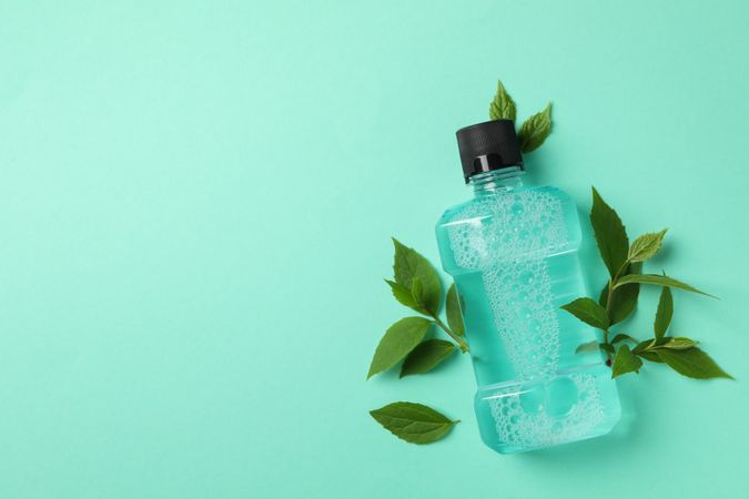 Mouthwash and leaves on mint background, space for text