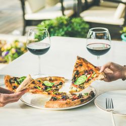 Two people taking opposite slices of freshly made pizza with red wine, square crop
