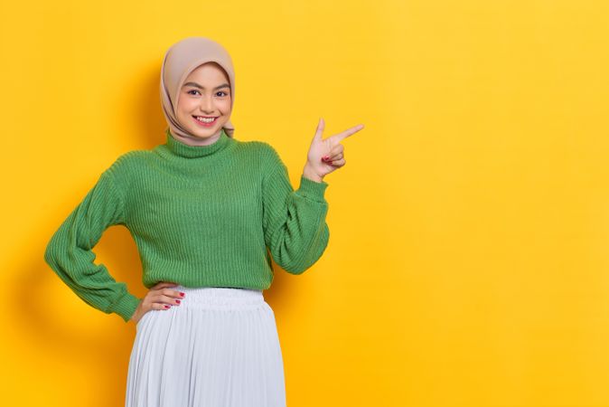 Excited woman in headscarf pointing to side with hand on hip