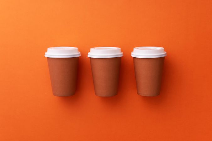 Three disposable coffee cups on orange background