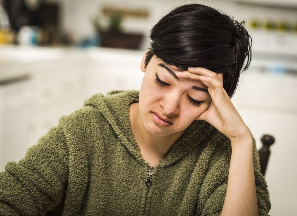 Depressed Young Woman Sitting Alone In Kitchen