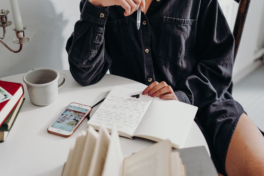 Cropped image of a person sitting at a table writing on a notebook