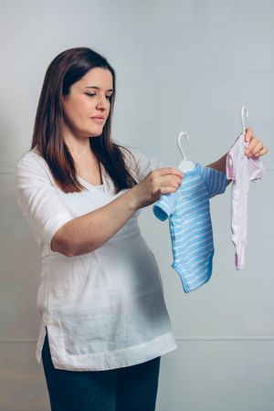 Pregnant woman choosing baby bodysuits