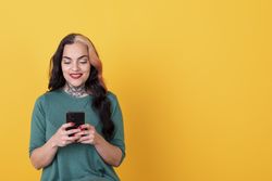 Portrait of a woman using smart phone over yellow background.  Copy space