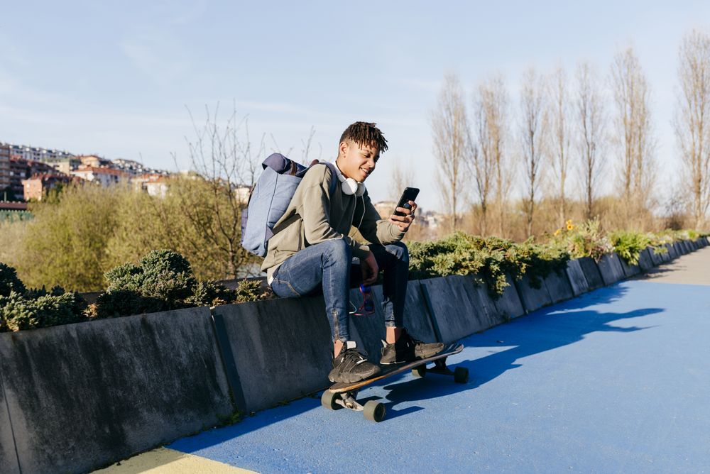 Young cheerful Black male sitting with skateboard
