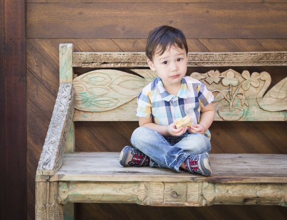 Cute Biracial Boy Sitting on Bench Eating Sandwich