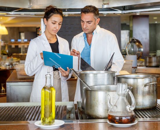 Coworkers checking results while testing food quality in canteen kitchen