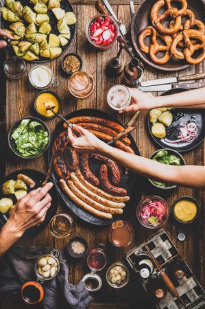 German sausages and pretzels displayed on wooden table with hands dipping food in mustard