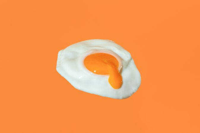 Fried egg minimalist on an orange background with egg yolk dripping