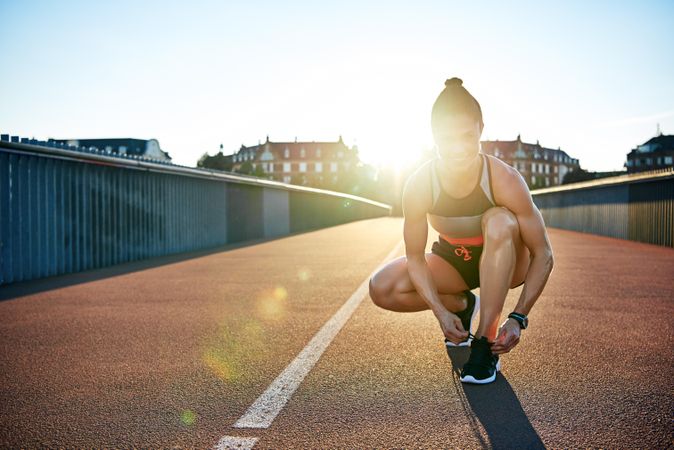 Athletic woman tying shoes on bridge with lens flare