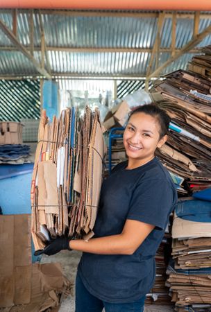 Young Hispanic Woman Smiling While Holding A Heavy Cardboard Pile
