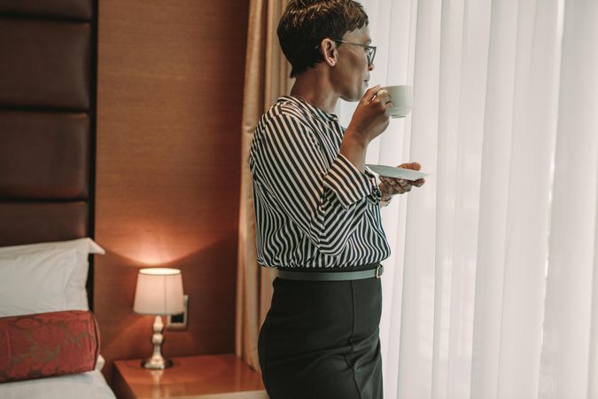 Businesswoman standing near in hotel room window with a cup of coffee
