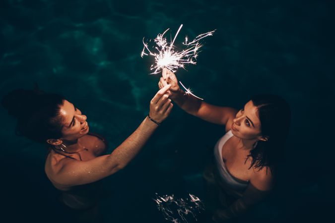 Cheerful friends burning sparkles near pool