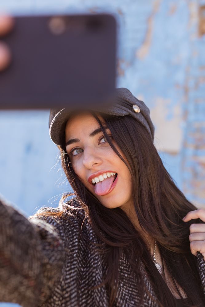 Charming Hispanic woman taking selfie near wall