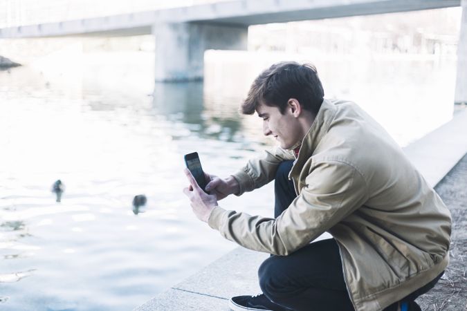 Man taking photos by lake with smartphone