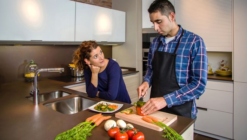 Woman talking to man as he cuts vegetables for dinner