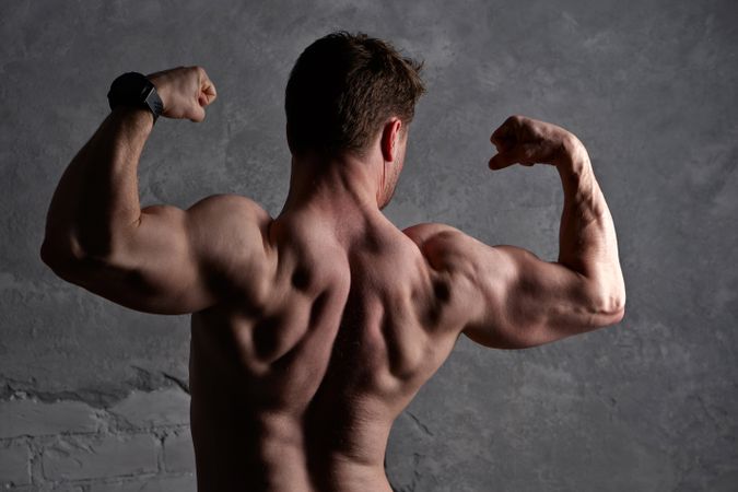 Muscular man flexing arms, back definition under dramatic lighting.