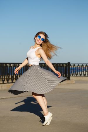 Happy female in striped skirt joyously dancing near water