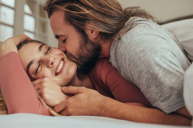 Couple in bed spending time together with man kissing his partner