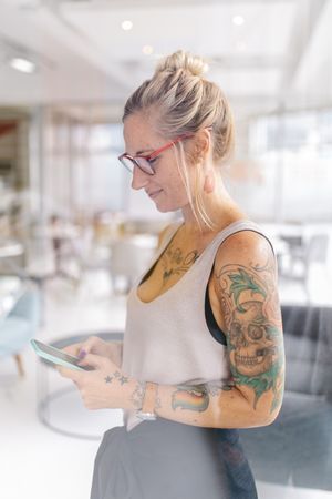 Tattooed woman looking down at her mobile phone in a bright modern office