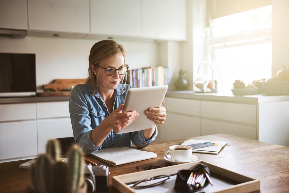 Woman holding and reading tablet at kitchen table