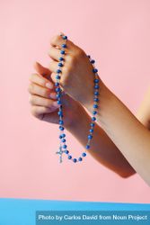 Hands holding rosary beads in pink room with blue table 0W1Mp4