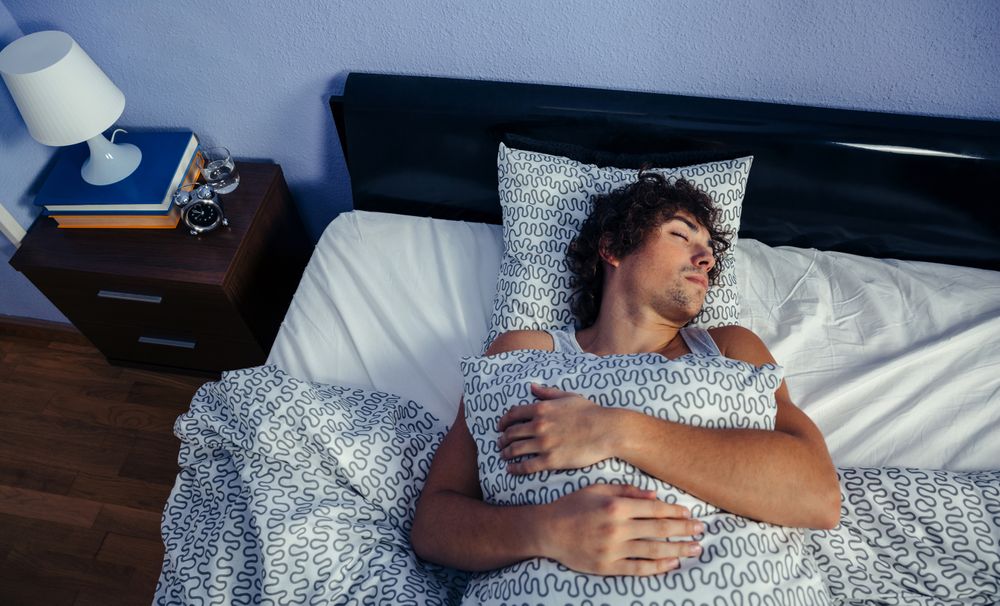 Man sleeping in bed at home holding pillow