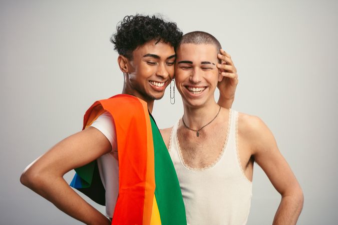 Cheerful couple with pride flag on light background